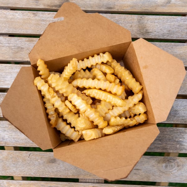 Crinkle-cut french fries in a brown paper take-out container on a wooden slatted table.