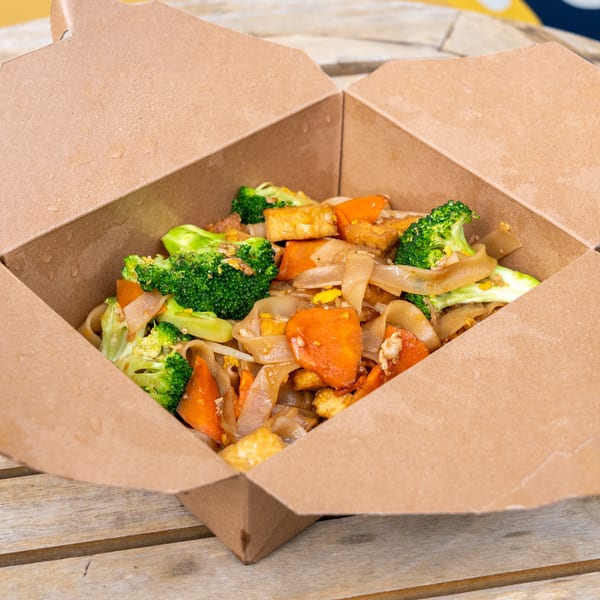 Takeout box filled with Pad See Ew, featuring wide noodles, broccoli, carrots, and tofu.