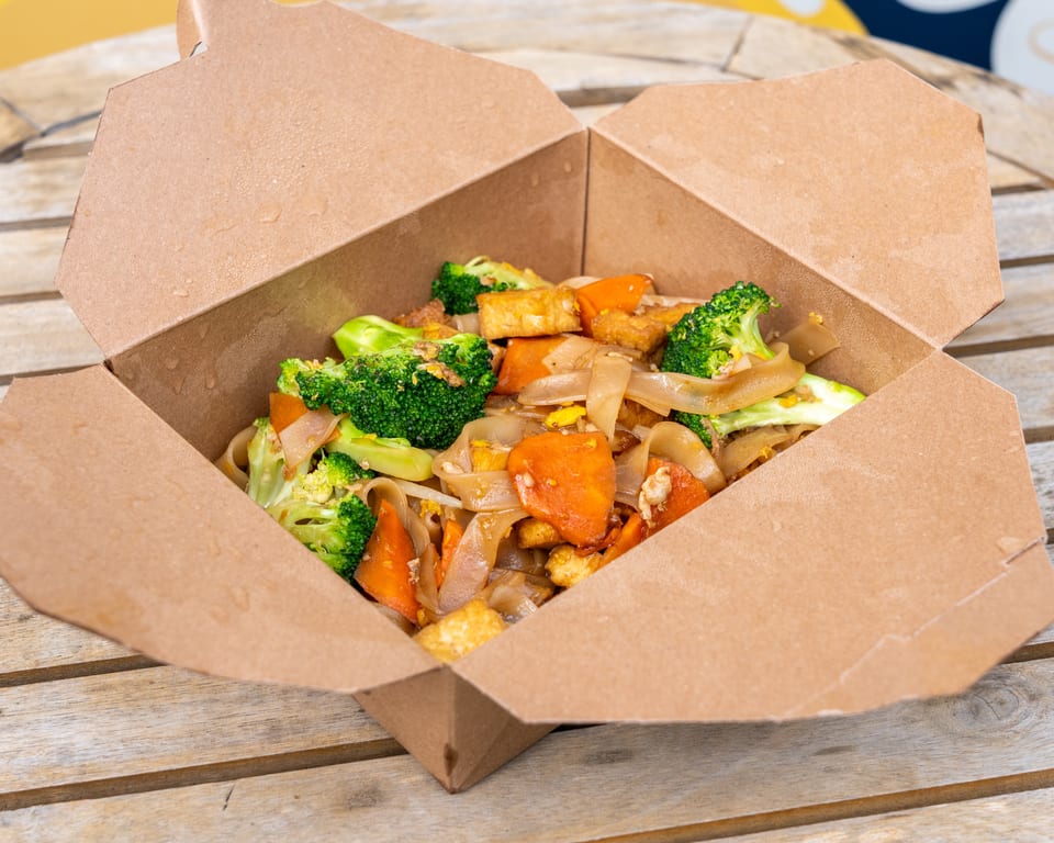 Takeout box filled with Pad See Ew, featuring wide noodles, broccoli, carrots, and tofu.