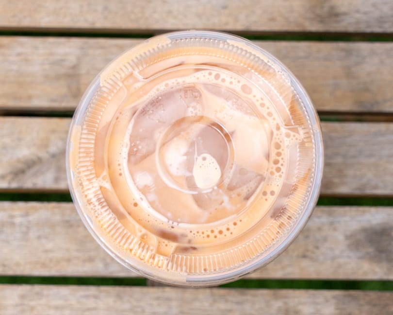 Overhead view of an iced Thai tea in a plastic cup with a lid on a wooden table.