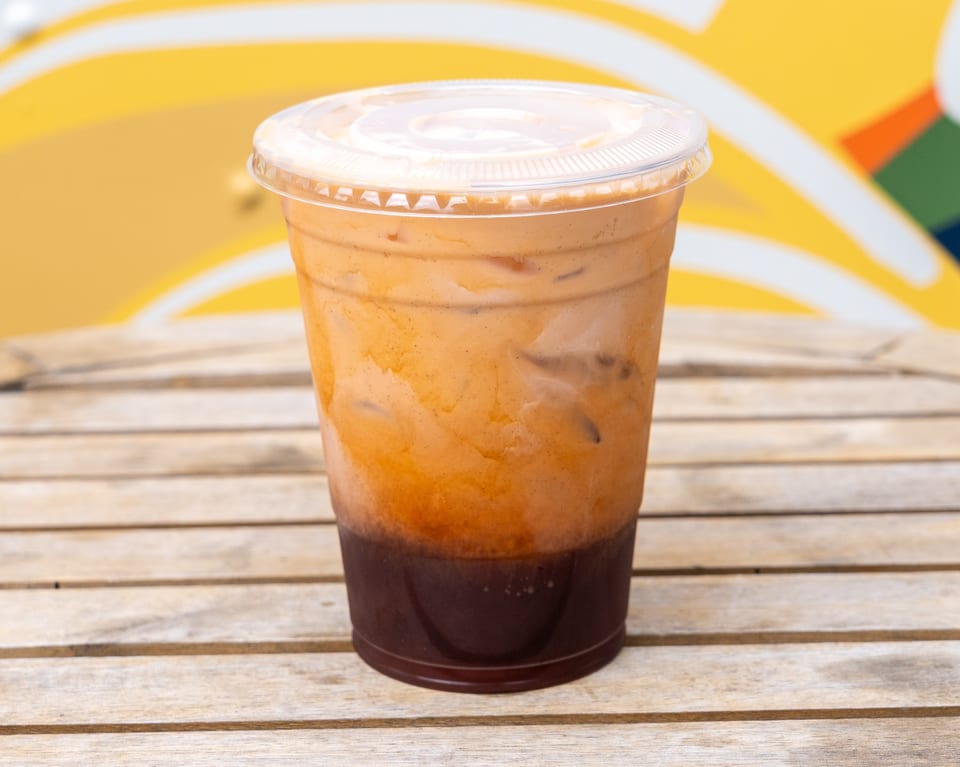 Iced Thai tea in a clear plastic cup on a wooden table with a colorful background.