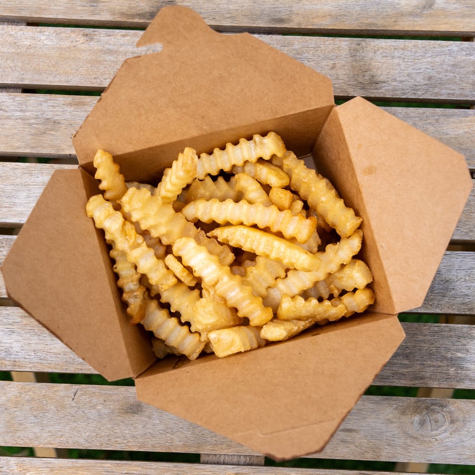 Crinkle-cut fries in a brown paper box, sitting on a wooden slatted table.