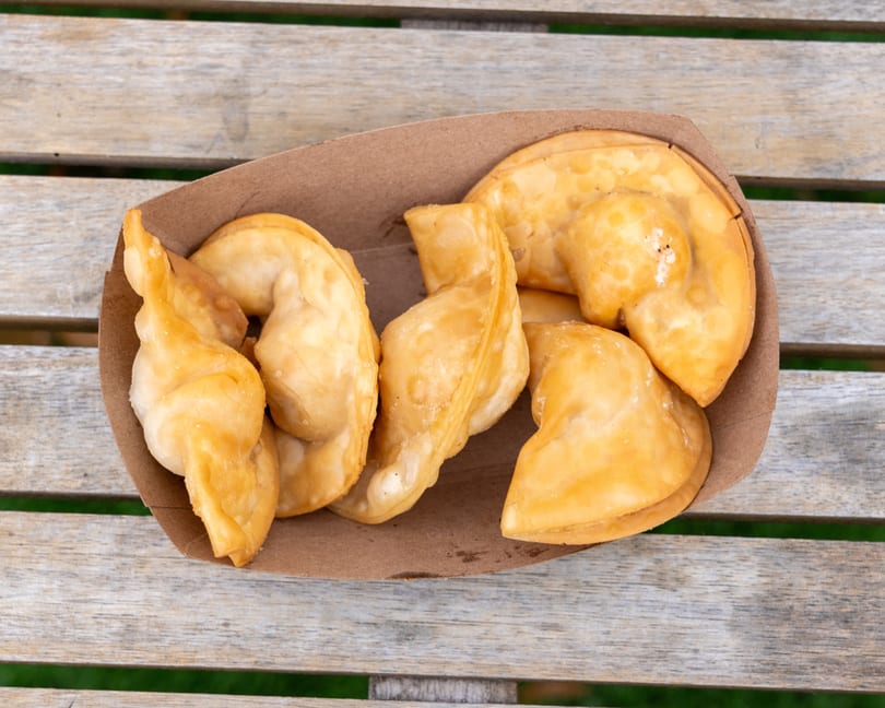 Golden-brown fried dumplings in a cardboard tray on a rustic wooden table.
