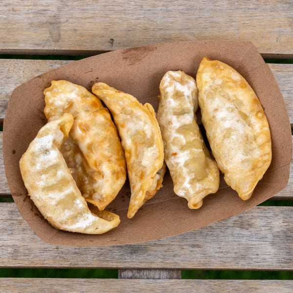 Five golden-brown fried dumplings in a brown paper tray on a rustic wooden table.