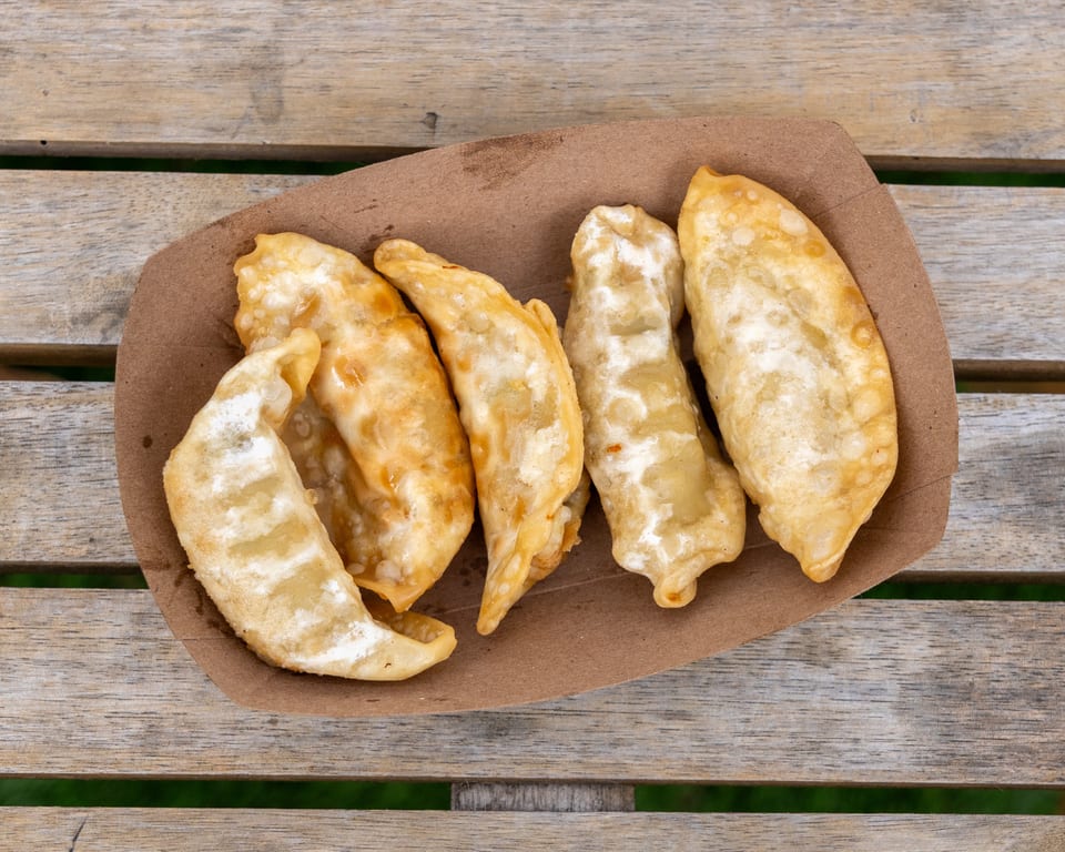 Five golden-brown fried dumplings in a brown paper tray on a rustic wooden table.