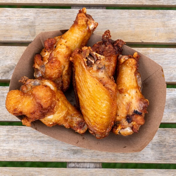 Crispy golden-brown chicken wings in a brown paper bowl on a rustic wooden table.
