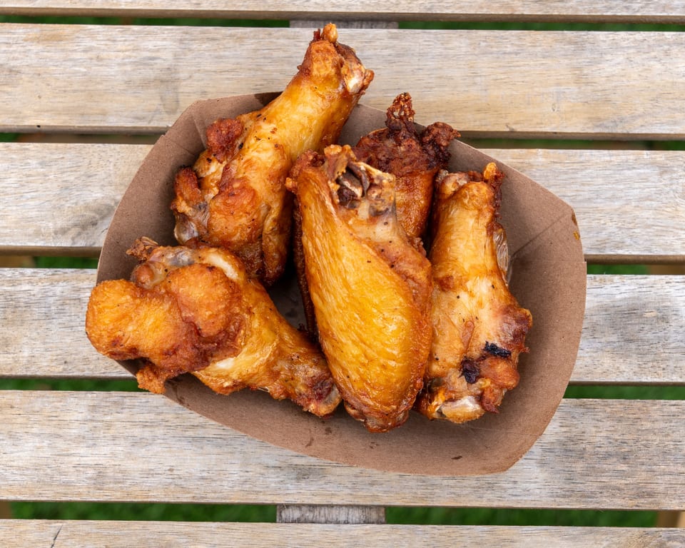 Crispy golden-brown chicken wings in a brown paper bowl on a rustic wooden table.