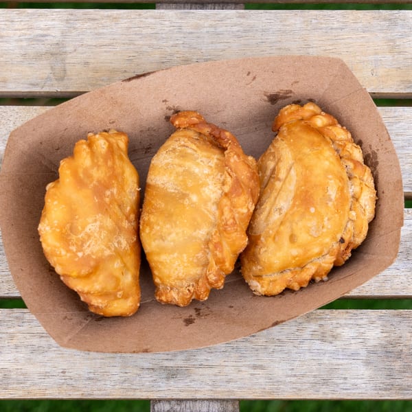 Three golden-brown curry puffs in a brown paper tray on a wooden table.
