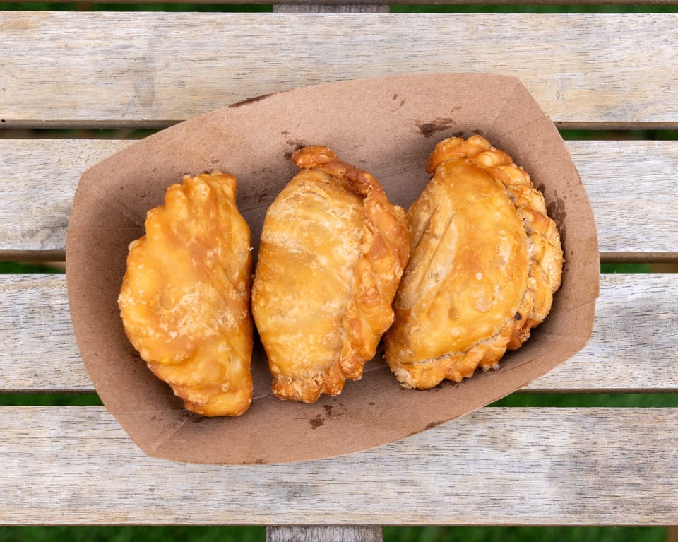 Three golden-brown curry puffs in a brown paper tray on a wooden table.