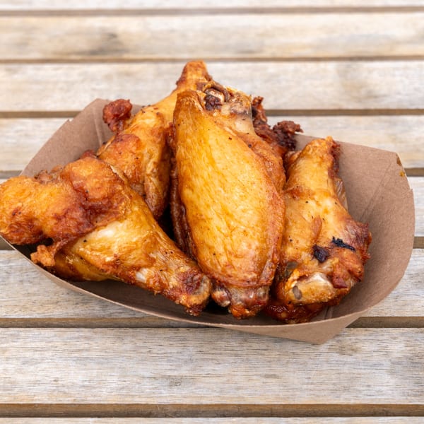 Crispy golden-brown chicken wings in a brown paper tray on a rustic wooden table.