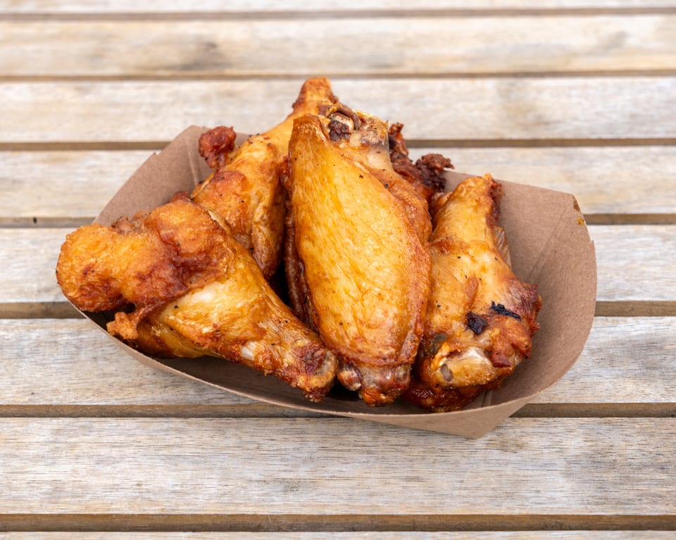 Crispy golden-brown chicken wings in a brown paper tray on a rustic wooden table.