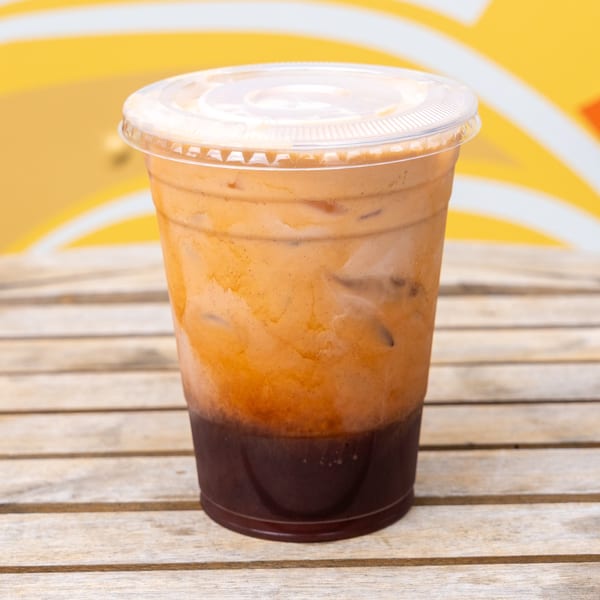 Iced Thai tea with a dark brown base and creamy orange top, on a wooden table.