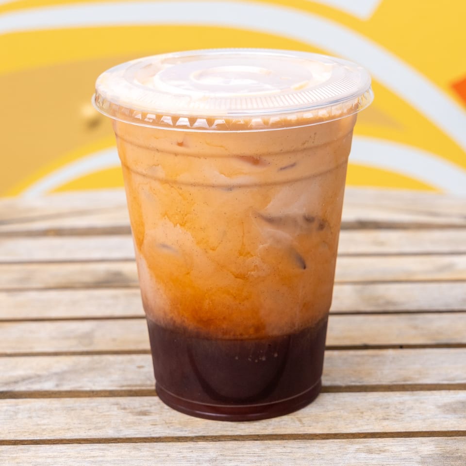 Iced Thai tea with a dark brown base and creamy orange top, on a wooden table.
