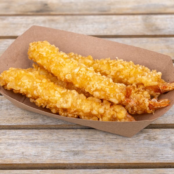 Golden-brown tempura shrimp in a brown paper tray on a rustic wooden table.